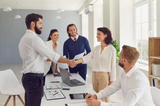Team of people in office shaking hands around a table