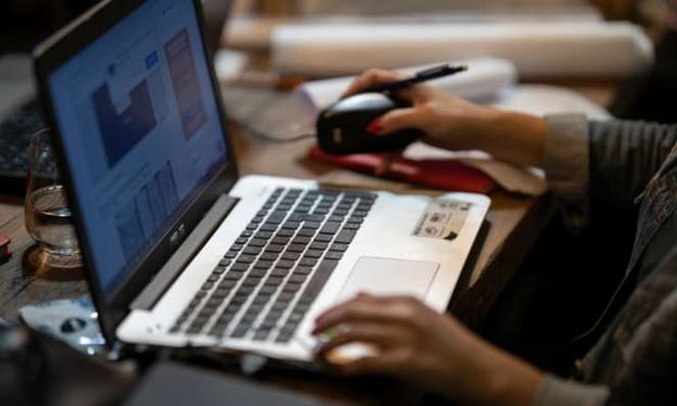 A laptop is open, and the screen shows data charts and images. One hand is on a mouse with a pen, and the other is resting on the laptop. 