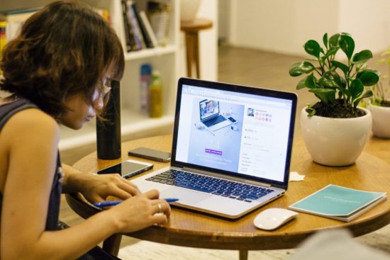 A girl in front of her laptop while holding a pen.