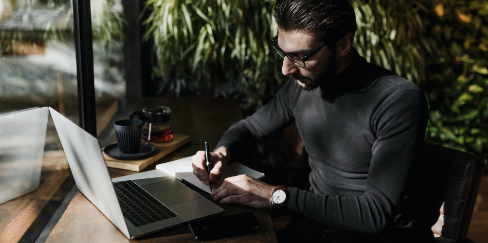 man making notes in front of laptop